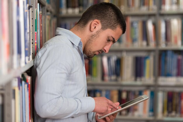 Nella biblioteca Studente maschio bello con il computer portatile ed i libri che lavorano in una profondità del campo poco profonda della biblioteca dell'università della High School