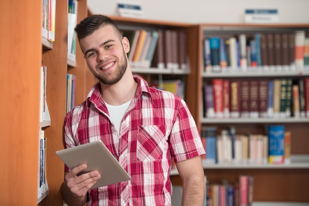 Nella biblioteca Studente maschio bello con il computer portatile ed i libri che lavorano in una profondità del campo poco profonda della biblioteca dell'università della High School