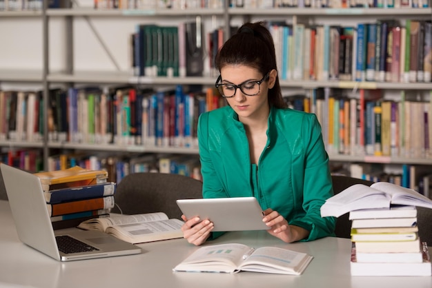 Nella biblioteca Studentessa graziosa con laptop e libri che lavorano in una biblioteca di scuola superiore o universitaria Profondità di campo poco profonda