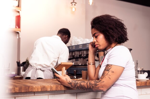 Nella caffetteria. Bella donna piacevole utilizzando il suo smartphone in attesa del caffè