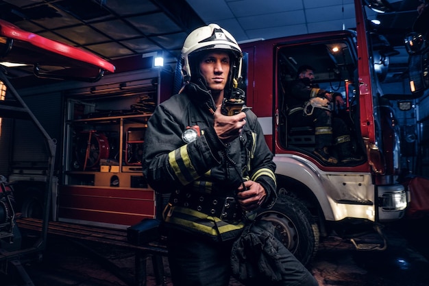 Nella notte sono arrivati i vigili del fuoco. Vigile del fuoco in uniforme protettiva in piedi accanto a un camion dei pompieri e parlando alla radio