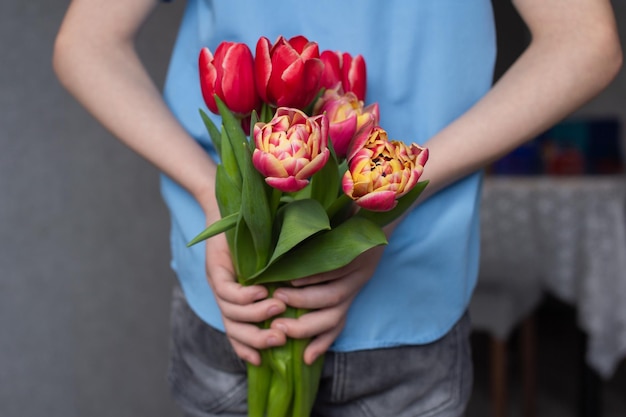 Nelle mani di un bambino ci sono tulipani rossi colorati ragazzo che nasconde fiori dietro la schiena