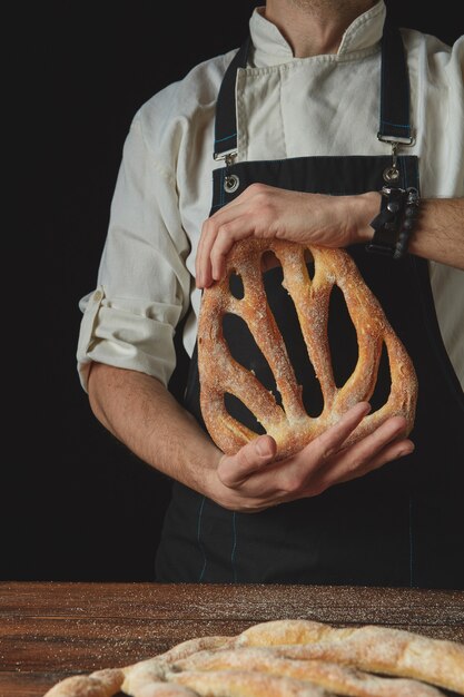 Nelle mani di un panettiere di fougas fresco biologico su uno sfondo scuro