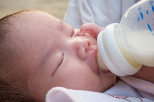 Neonata asiatica felice sveglia con la bottiglia di latte