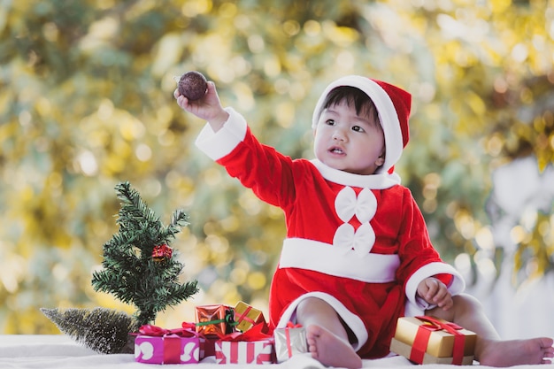 Neonata asiatica sveglia che indossa il vestito di Santa con i bei contenitori di regalo sulla celebrazione di Natale