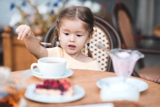 Neonata carina che mangia torta di frutta e beve tè al bar