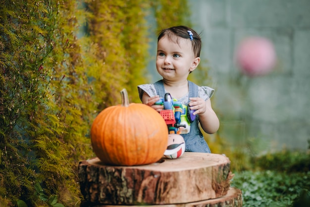 Neonata carina e divertente in piedi accanto ai pedoni decorativi e alla zucca nel loro cortile e sorridente