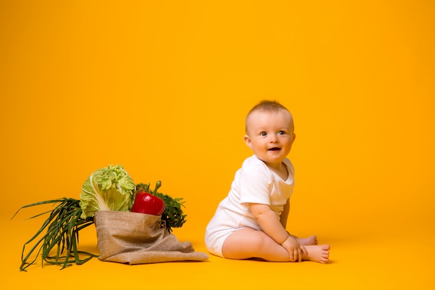 Neonata che si siede con la borsa delle verdure su giallo