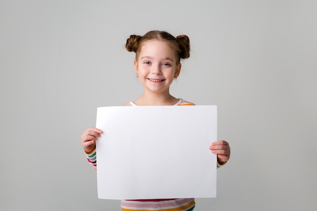 Neonata che tiene un foglio bianco Bambina sveglia con un foglio di carta bianco Priorità bassa blu Spazio per testo Una bambina tiene un pezzo di carta vuoto