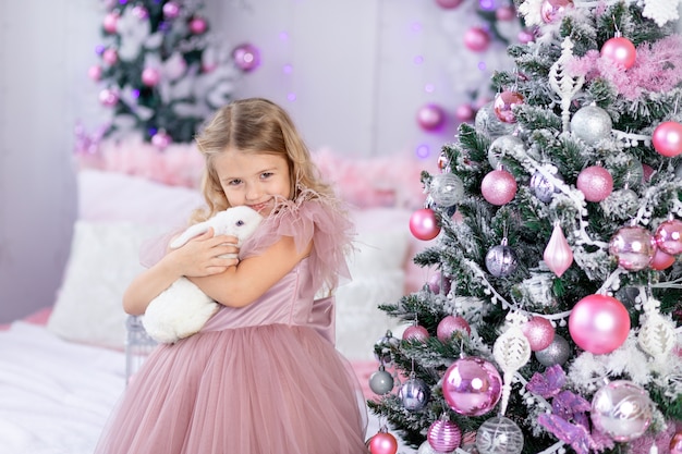 Neonata con coniglio all'albero di Natale in un bellissimo vestito rosa, Capodanno e concetto di Natale