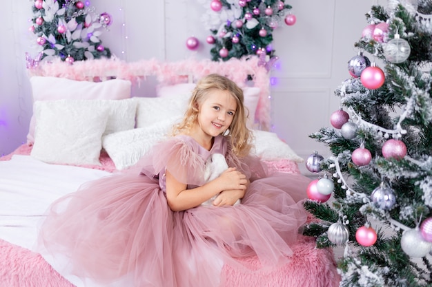 Neonata con coniglio all'albero di Natale in un bellissimo vestito rosa