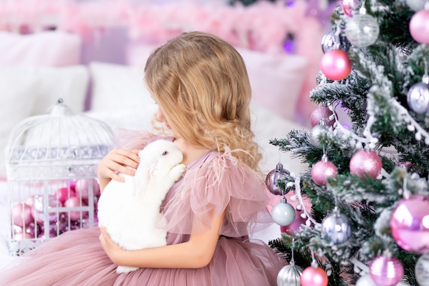 Neonata con coniglio all'albero di Natale in un bellissimo vestito rosa