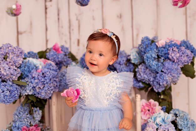 Neonata felice in un vestito in studio su uno sfondo bianco con fiori di ortensie rosa e blu