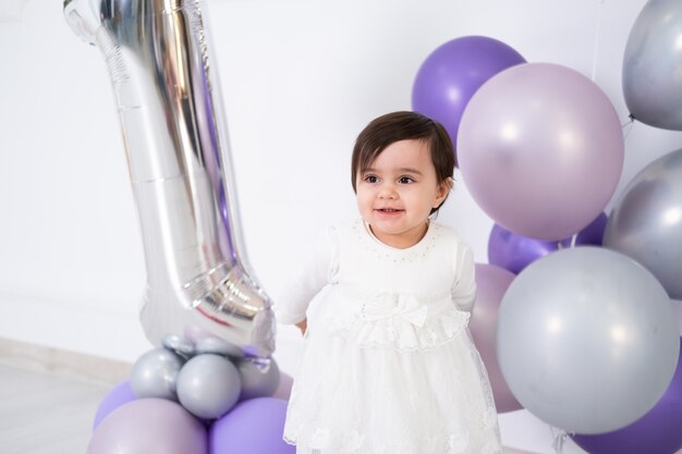 Neonata in vestito bianco che celebra il suo primo compleanno con torta e palloncini.