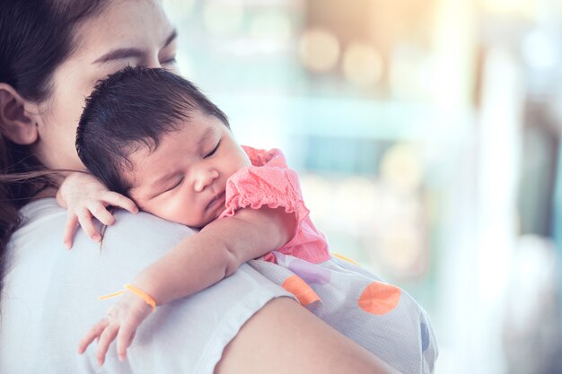 Neonata sveglia asiatica sveglia che dorme sulla spalla della madre.