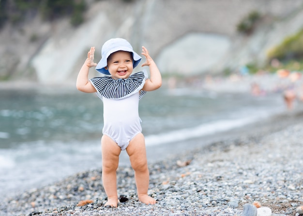 Neonata sveglia in piedi sulla costa del mare in un costume da bagno bianco