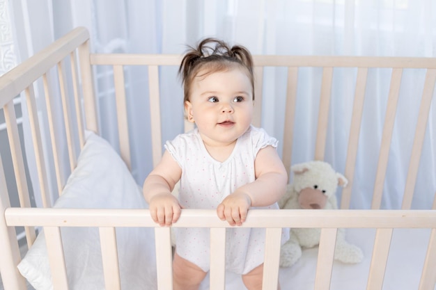 Neonata sveglia nella culla nella scuola materna nel ritratto della tuta bianca