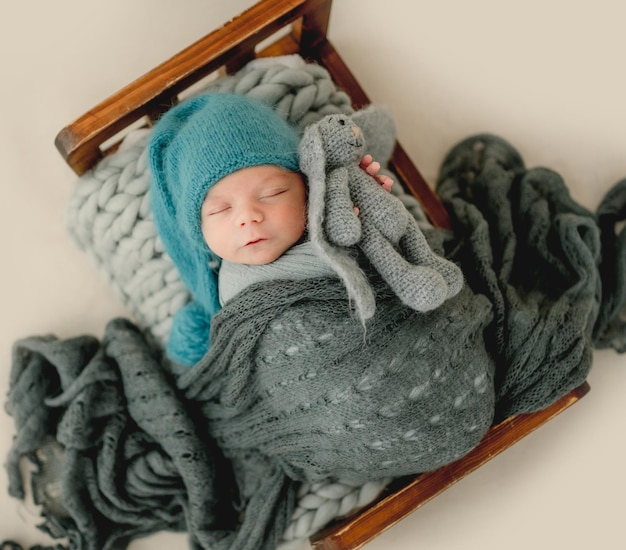 Neonato che indossa un cappello lavorato a maglia che dorme nel lettino e tiene in mano un coniglietto. Ritratto in studio di bambino bambino bambino carino