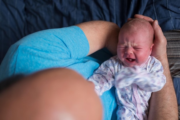 Neonato che piange sulle mani di suo nonno.