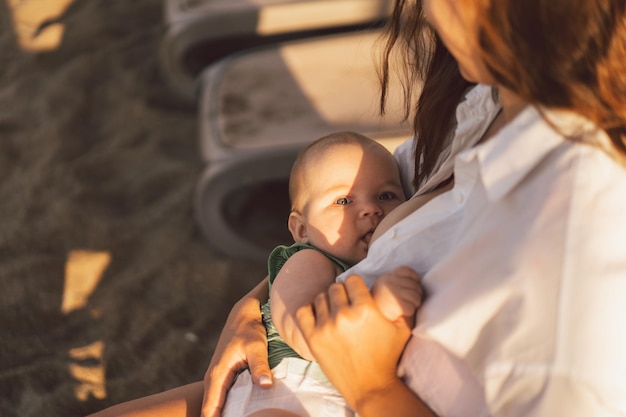 Neonato che succhia il latte dal seno delle madri sulla spiaggia