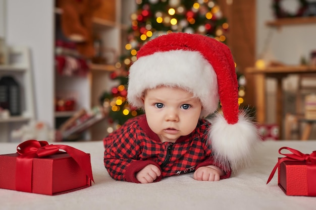 Neonato di Natale in cappello della Santa su fondo dell'albero di Natale con i regali.