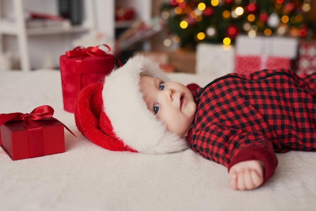 Neonato di Natale in cappello della Santa su fondo dell'albero di Natale con i regali.