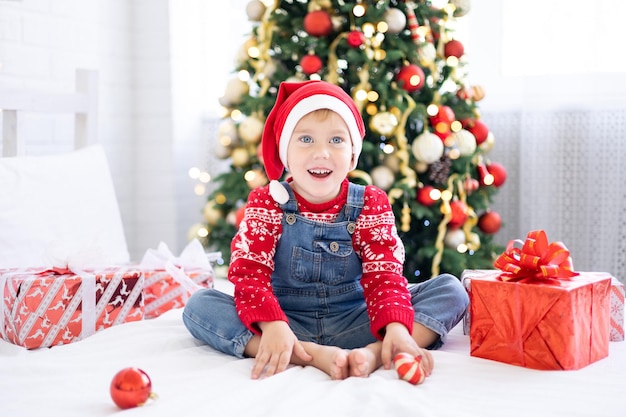 Neonato divertente felice con i regali a letto la mattina di Natale sullo sfondo dell'albero di Natale, il concetto di vacanze, natale, capodanno