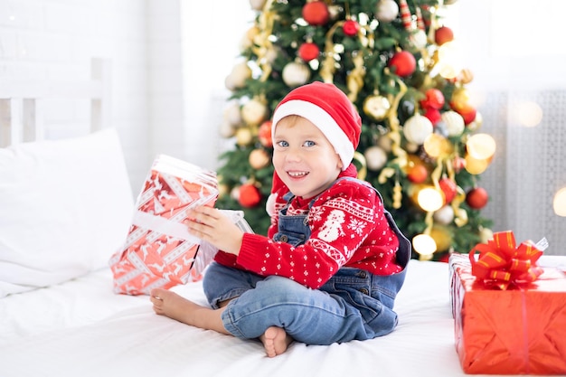 Neonato divertente felice con i regali a letto la mattina di Natale sullo sfondo dell'albero di Natale, il concetto di vacanze, natale, capodanno