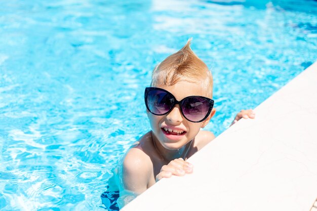 Neonato felice in occhiali da sole in una piscina di acqua blu, il concetto di vacanze estive e viaggi