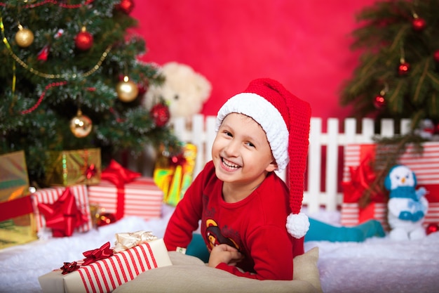 Neonato in cappello di Santa che sembra ampiamente sorridente. la stanza è decorata con luci di Natale tutte a luci.