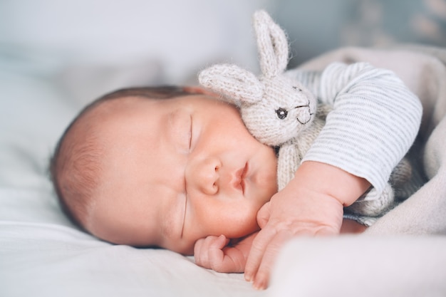 neonato ragazzo di una settimana che dorme pacificamente con un simpatico peluche nella culla in uno sfondo di stoffa