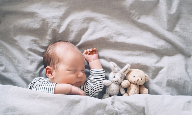 neonato ragazzo di una settimana che dorme pacificamente con un simpatico peluche nella culla in uno sfondo di stoffa