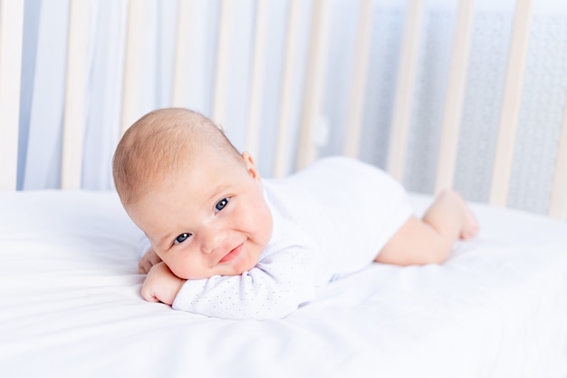 Neonato sorridente sulla pancia nella culla sul letto di cotone a casa, concetto di bambino sano healthy