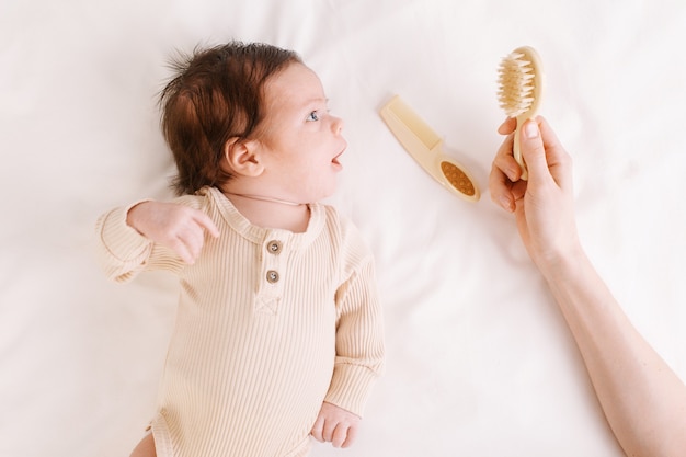 Neonato su un letto bianco con pettini, cura del bambino e igiene vista dall'alto