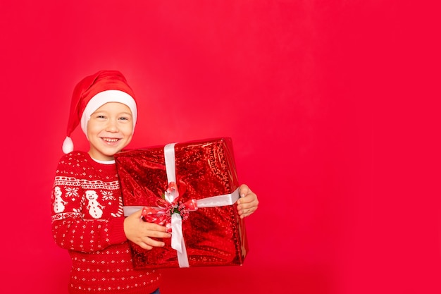 Neonato su uno sfondo rosso isolato con un regalo in un cappello da Babbo Natale