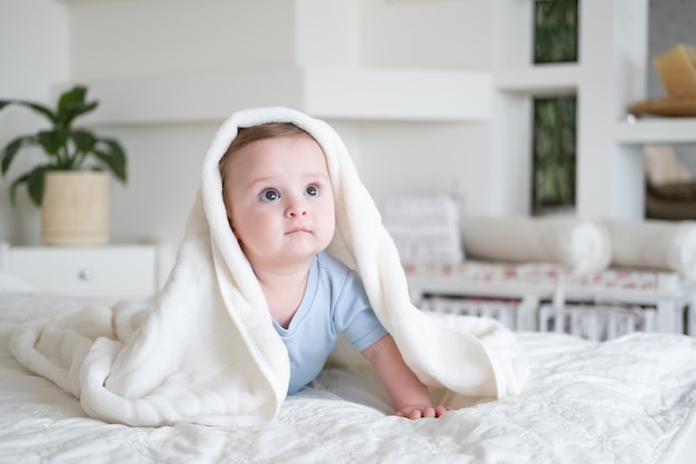 Neonato sveglio 6 mesi in tuta blu sorridente e sdraiato sul letto con plaid bianco a casa.