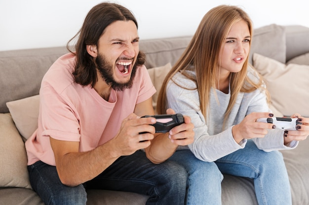 nervosa giovane coppia di innamorati sul divano gioca ai videogiochi con il joystick in casa.