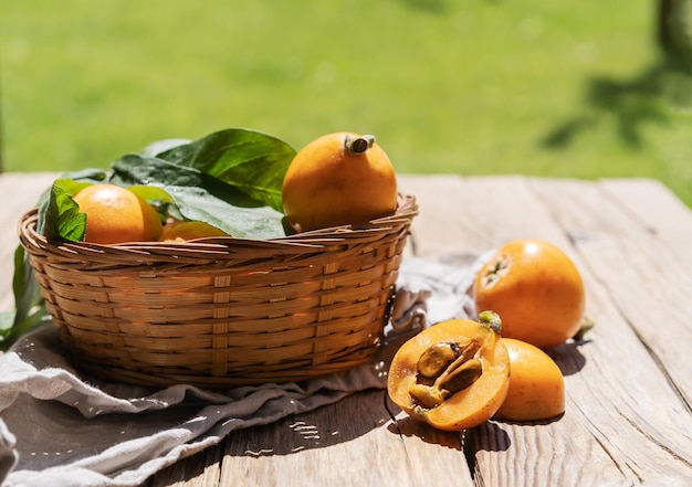 Nespola frutti in cestino con foglie e uno viene tagliato su un tavolo di legno in giardino