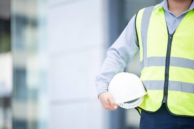 Nessun volto Persona irriconoscibile Torso ingegnere lavoratore o architetto che tiene in mano progetto e elmetto protettivo in plastica bianca su sfondo sfocato Spazio vuoto per la copia di oggetti di iscrizione