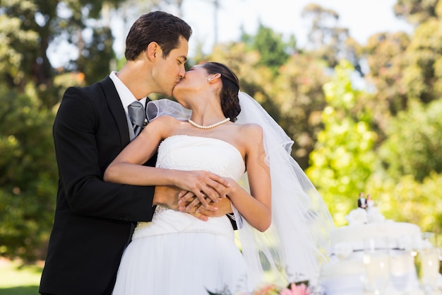 Newlywed baciare oltre a torta nuziale al parco