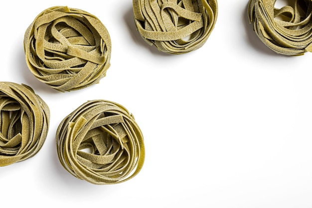 Nidi di pasta di tagliatelle di spinaci verdi su sfondo bianco ripresi dall'alto con spazio di copia