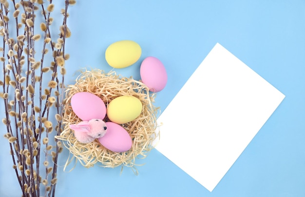 Nido con uova di Pasqua rami di salice e un foglio di carta bianco su sfondo blu