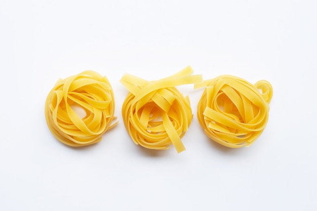 Nido di tagliatelle italiano crudo della pasta su fondo bianco