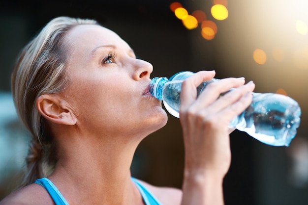 Niente ha un sapore migliore dell'acqua dopo un allenamento intenso Inquadratura di una donna matura che beve acqua da una bottiglia all'aperto