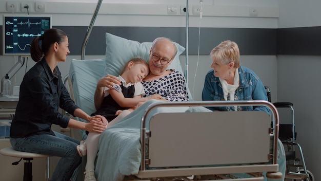 Nipote che abbraccia il nonno malato durante la visita nel letto del reparto ospedaliero. Bambina che visita un uomo anziano malato, dando supporto e aiutando con il recupero. Paziente in pensione che gode dell'assistenza dei visitatori.