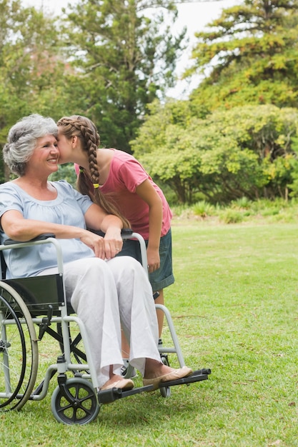 Nipote che bacia la guancia della nonna in sedia a rotelle