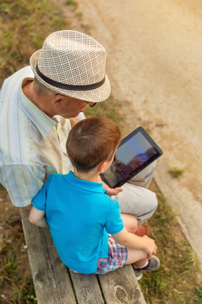 Nipote che insegna a suo nonno a usare una tavoletta elettronica su una panchina del parco. Concetto di valori di generazione.