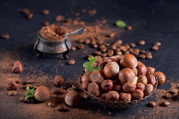 Nocciola, chicchi di caffè e cacao in polvere su sfondo scuro. Ingredienti per cucinare dolci al cioccolato fatti in casa. Concetto di dolci e dolci