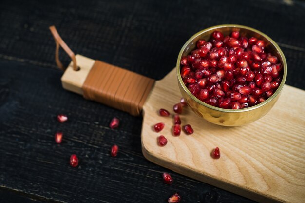 Noccioli di melograno in una ciotola su un tagliere di legno.