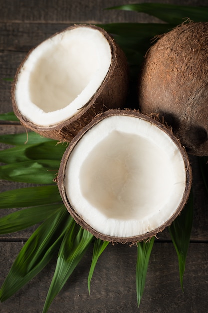 Noce di cocco con le foglie verdi su un fondo di legno.